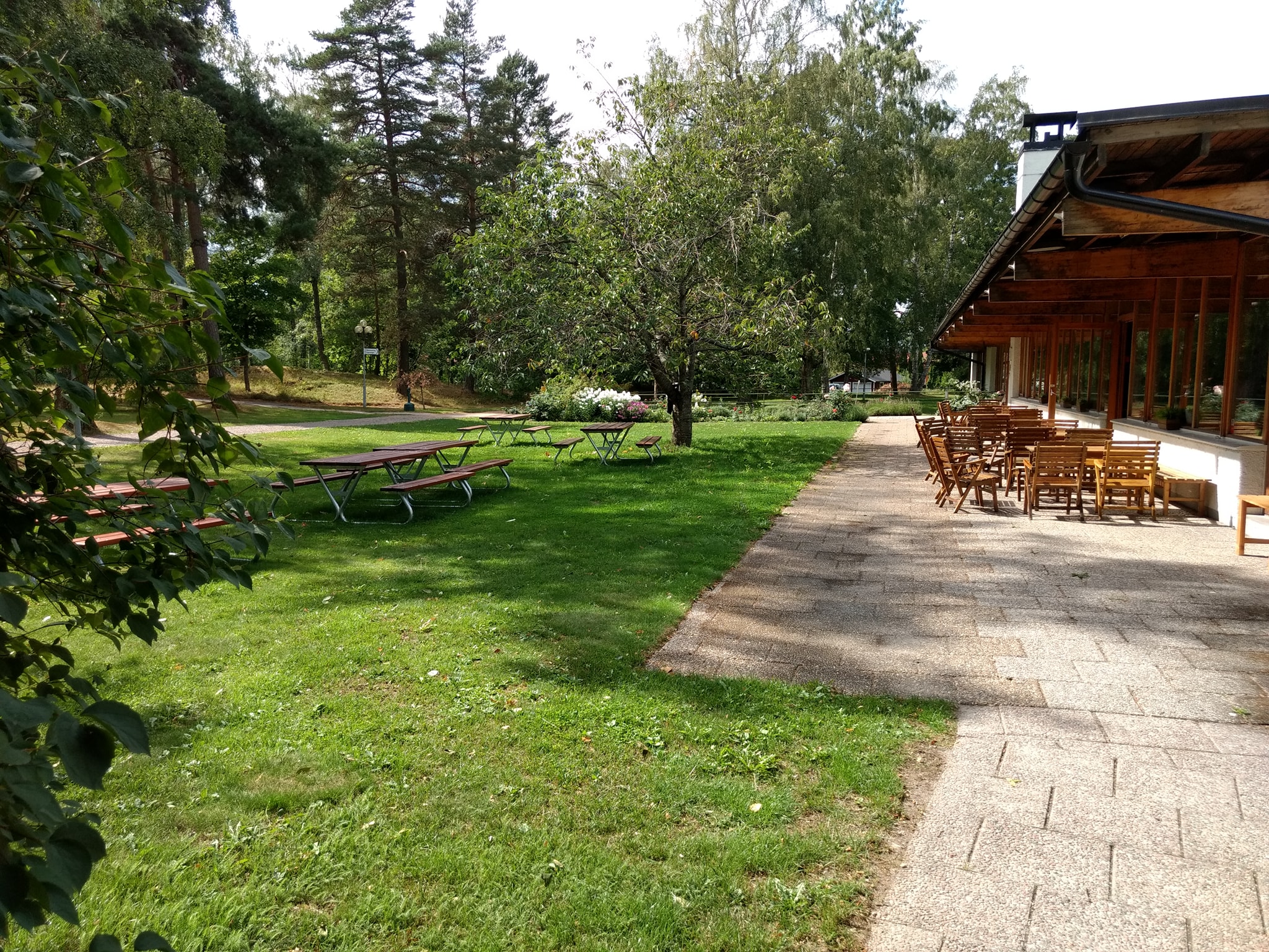 Hagabergs restaurangs uteservering med bord och stolar omgivet av gräs och träd.